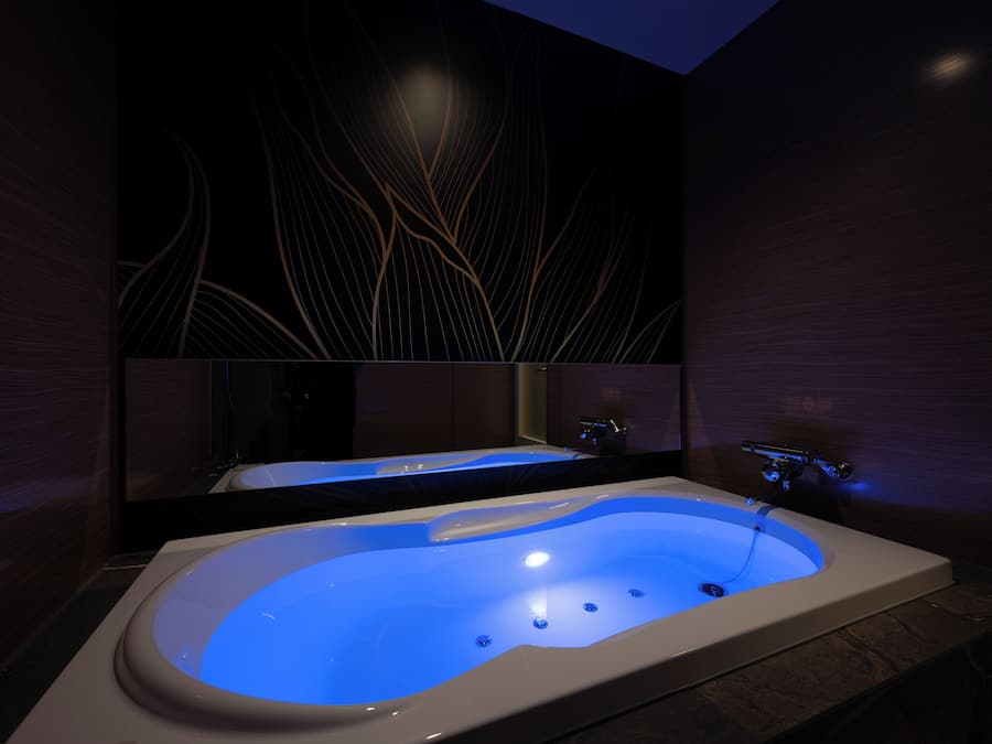 A modern bathroom with a large bathtub, a mirror, and a wall with a leaf pattern.