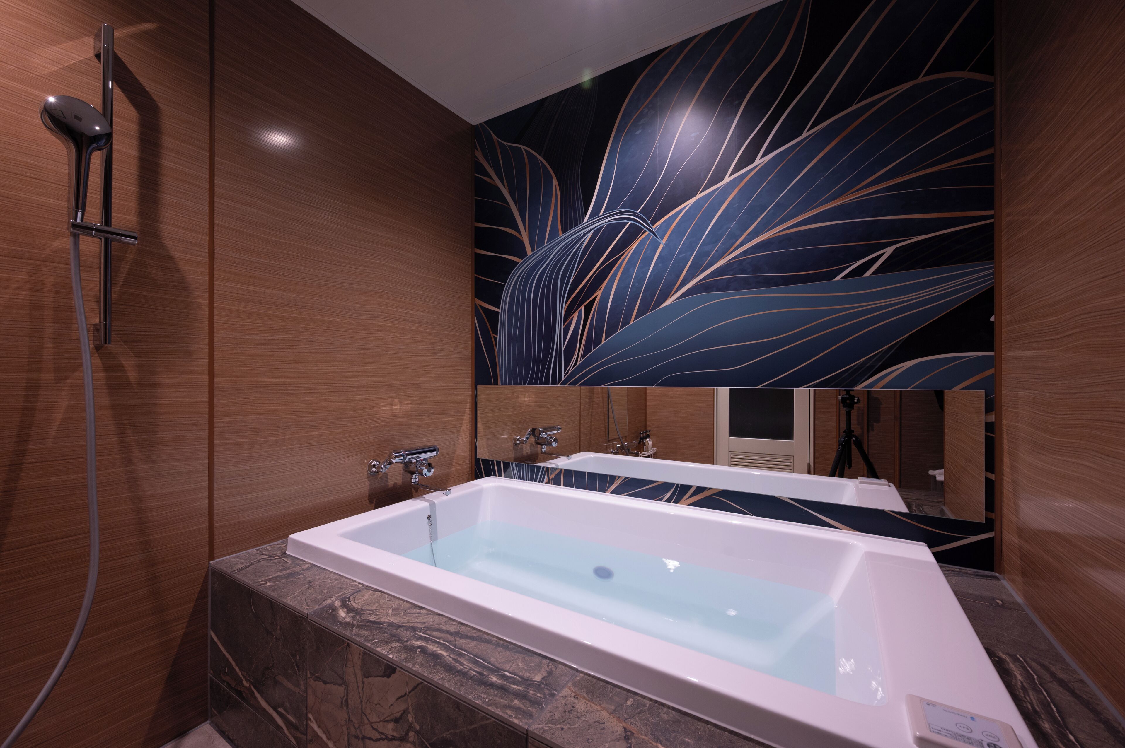 A modern bathroom with a large bathtub, a shower, and a wall with a leaf pattern.