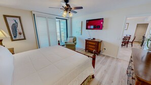 A hotel room with a bed, a ceiling fan, a TV, a chair, a dresser, and a dining area. - Mainsail 136 3 Bedroom Condo (Miramar Beach)