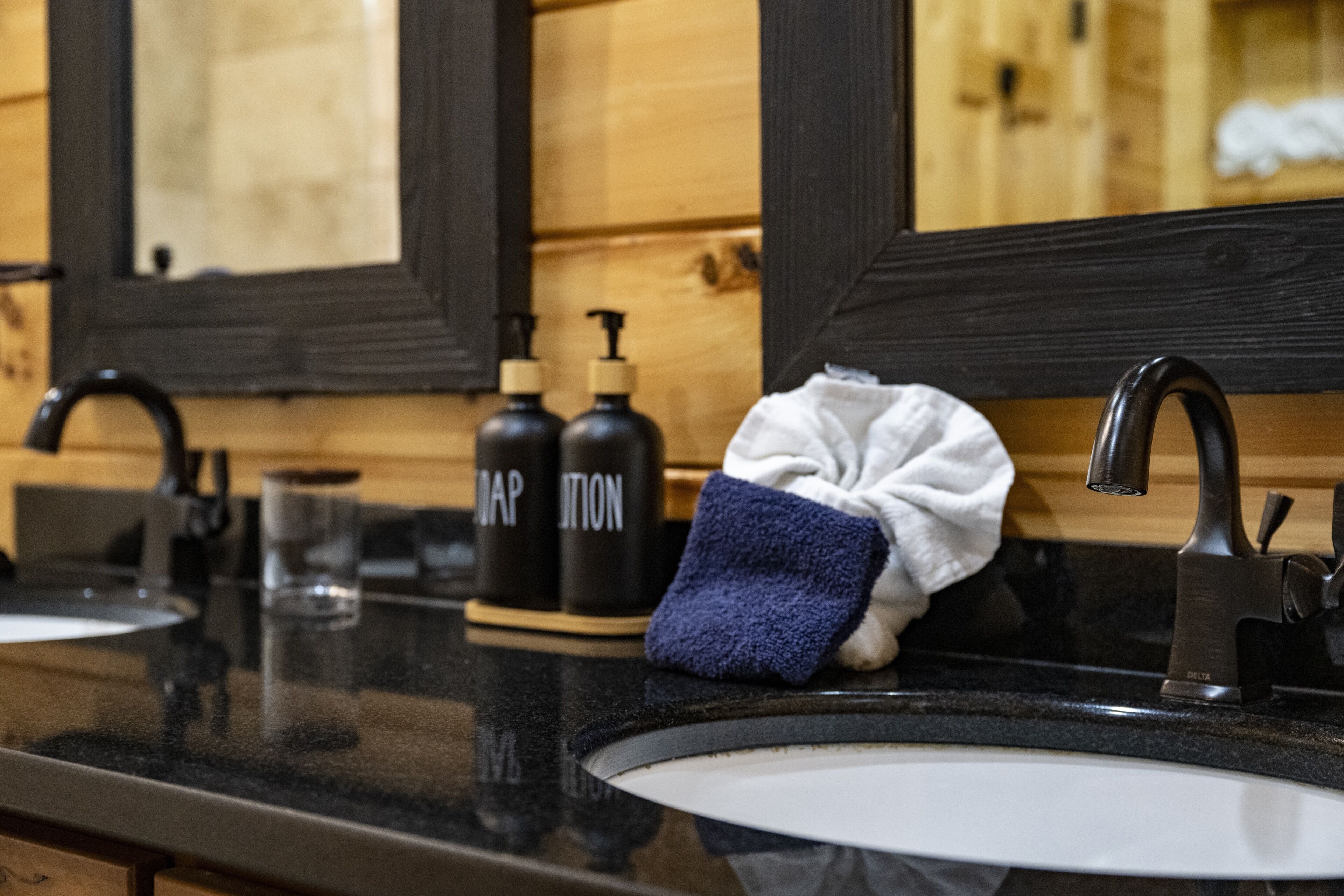 Un baño con encimera negra, lavabo blanco, espejo y dos botellas etiquetadas 'SOAP' y 'SOAP'.