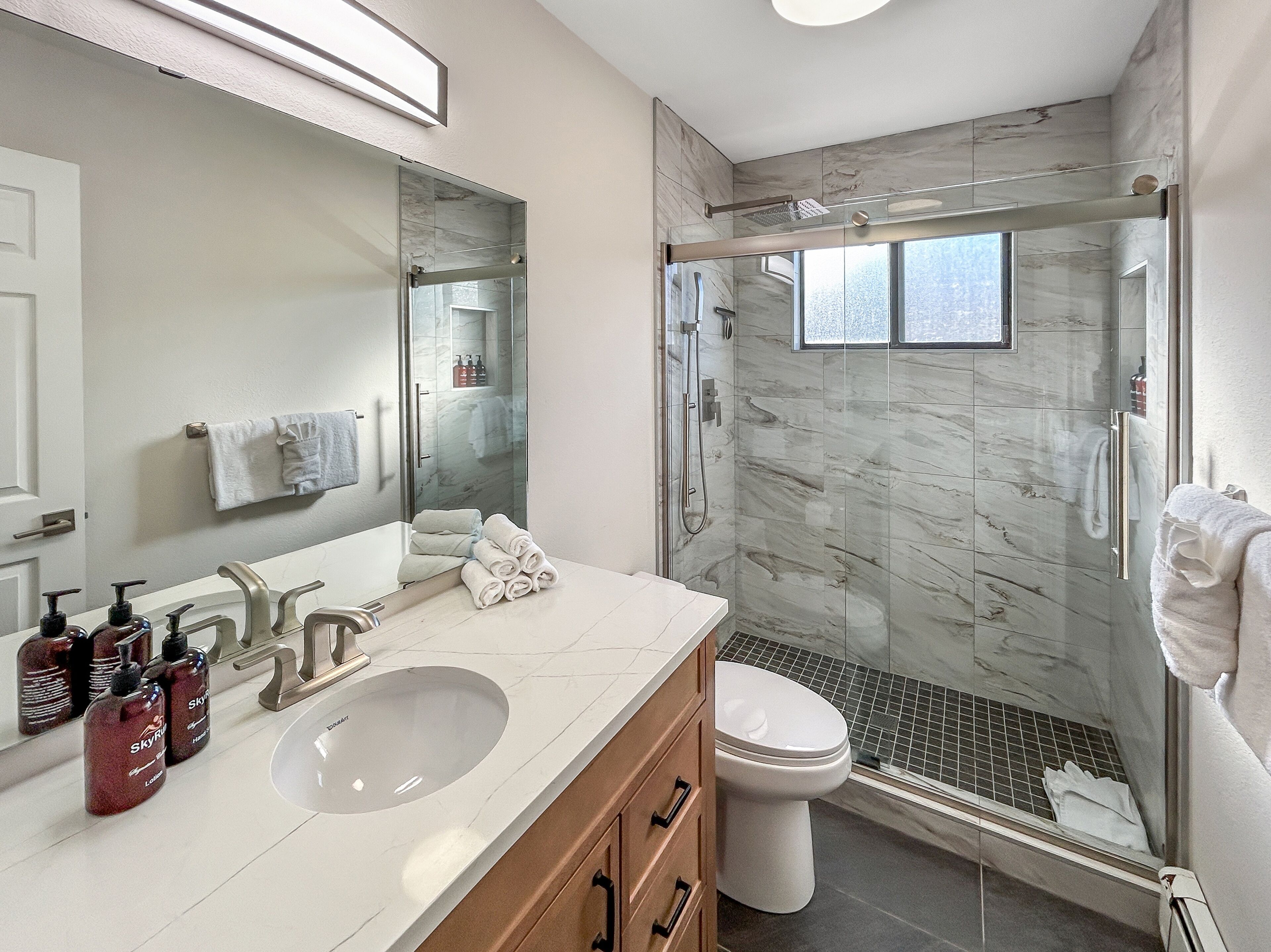 Een moderne badkamer met een douchecabine van glas, een grote spiegel en een wastafel met toiletartikelen.