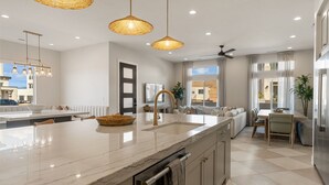 A modern kitchen with a marble countertop, a built-in sink, and a dining area with a table and chairs. - Sunset Pearl At Desert Color 8 Bedroom Townhouse (St. George)
