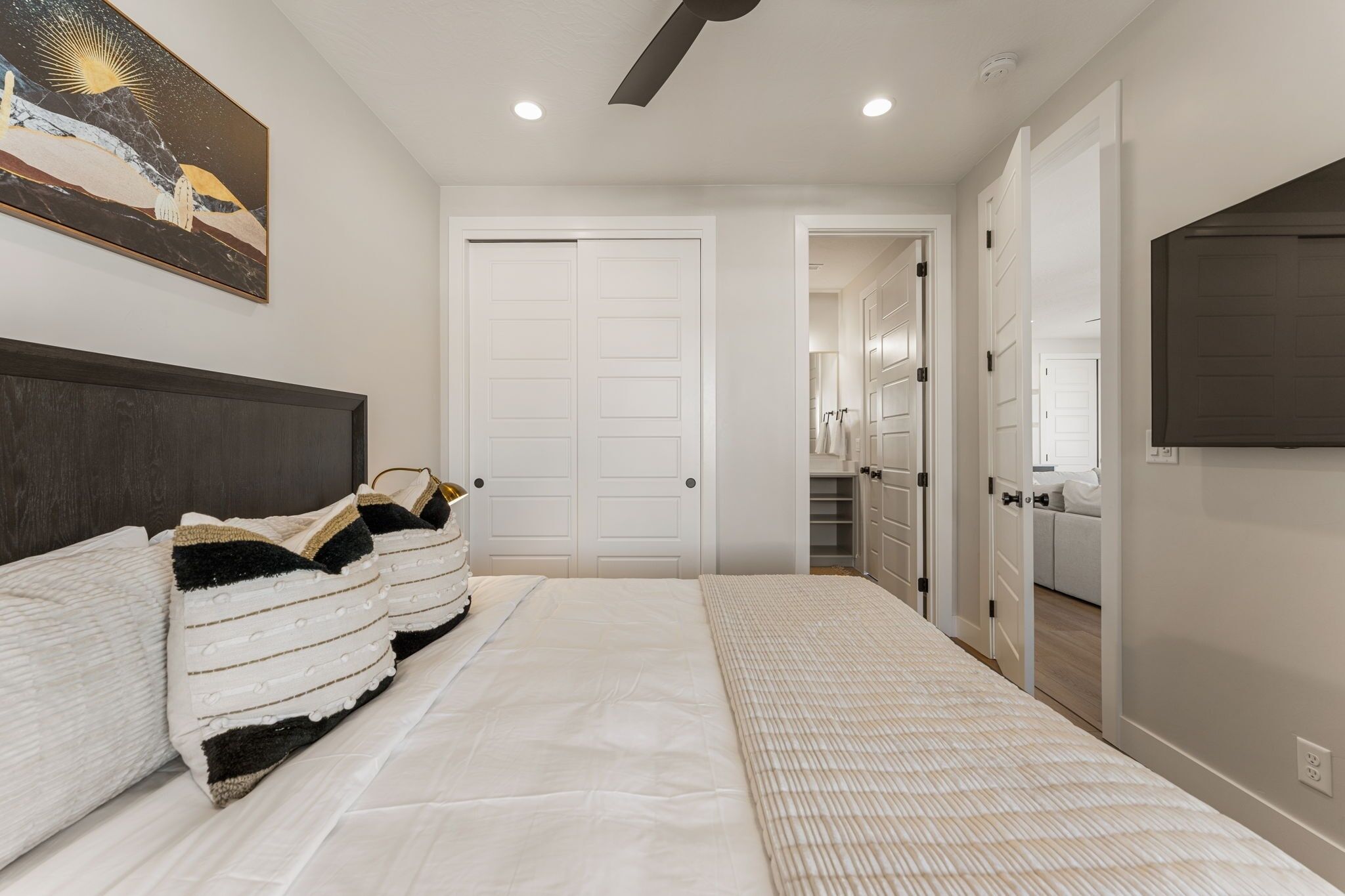 A bedroom with a large bed, a headboard, a painting on the wall, and a closet with a mirror.