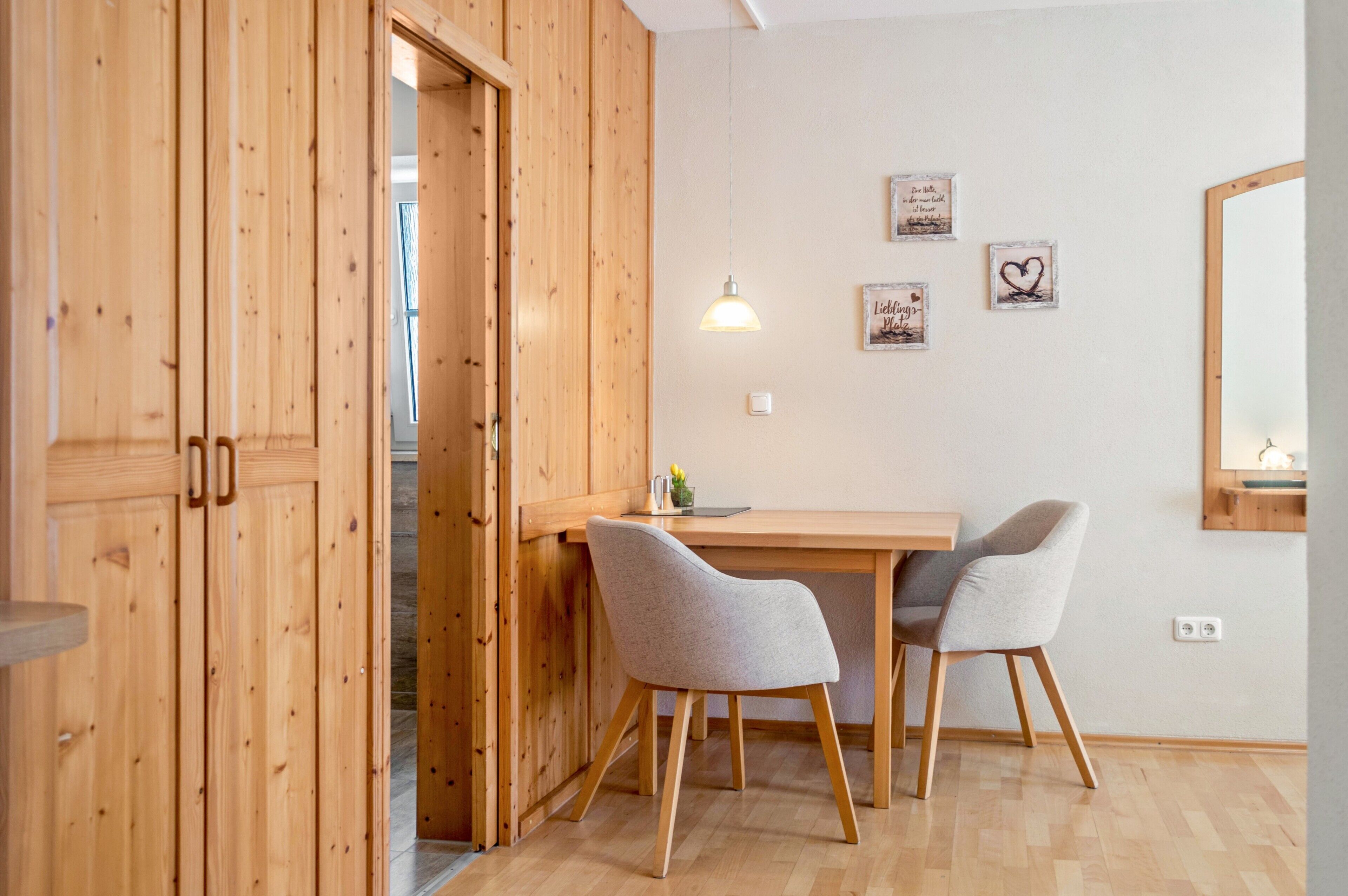 A room with wooden walls, a wooden desk, two grey chairs, a hanging lamp, and a mirror on the wall.