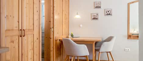 Une pièce aux murs en bois, avec un bureau en bois, deux chaises grises, une lampe suspendue et un miroir accroché au mur.