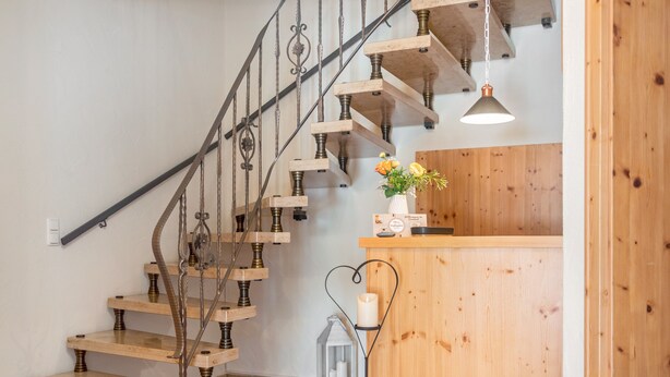 Un escalier en bois avec des balustrades en métal et un comptoir d’accueil en bois orné d’un vase de fleurs.