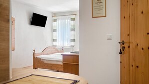 Une chambre à coucher avec un lit en bois, un téléviseur fixé au mur, une fenêtre avec des rideaux et une porte avec un cadre en bois.