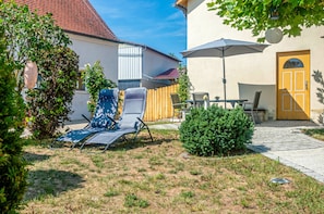 A courtyard with a lawn, a blue lounge chair, a wooden fence, a door, and a table with chairs.