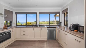 A modern kitchen with a view of the sea, a dishwasher, and a coffee maker. - Ohana Oasis, Kiama, South Coast (Kiama)