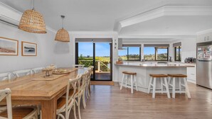 A modern kitchen with a large island, white cabinetry, and a view of the outdoors. - Ohana Oasis, Kiama, South Coast (Kiama)