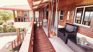 A wooden balcony with a swing chair, a small table with a potted plant, and a view of the surrounding area. - Charming Villa with Atlantic Ocean view (Cabrera)