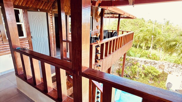 A wooden balcony with a view of a swimming pool and lush greenery. - Charming Villa with Atlantic Ocean view (Cabrera)
