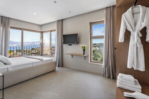 A modern hotel room with a large bed, a TV, a wooden shelf with a vase, and a balcony with a view of the mountains. - Villa Altamare (Splitska)