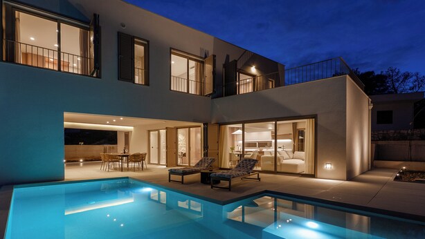 Une maison moderne à deux étages, dotée d’une piscine, d’un espace salon extérieur et de grandes fenêtres.