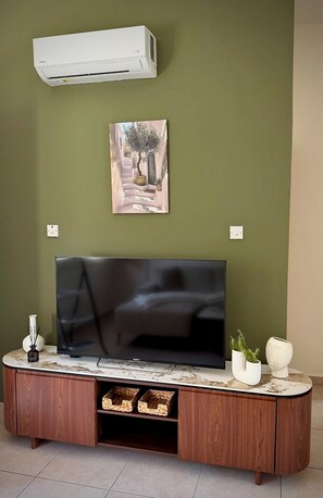 Ein Flachbildfernseher auf einer Holzkabine mit Marmorplatte, eine Wandklimaanlage und ein gerahmtes Bild über dem Fernseher.