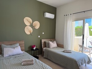 A hotel room with two beds, a small table with a vase of flowers, and a sliding glass door to an outdoor area. - The sea, restaurants and shopping facilities can be  on foot in appr. 15 min. (Paphos)