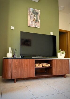 Een flatscreen televisie op een houten tv-meubel, met een vaas en een potplant ernaast.
