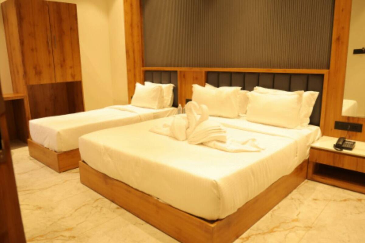 A hotel room with two single beds, wooden headboards, a large mirror, and a bedside table with a lamp.