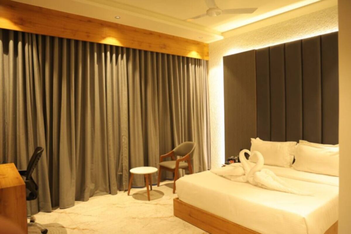 A hotel room with a bed, a chair, a small table, and a curtain.