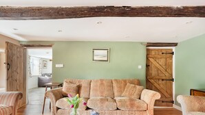 A cozy living room with a patterned sofa, a wooden coffee table with a vase of flowers, and a rustic wooden door. - Middle Dean Farmhouse (Barnstaple)