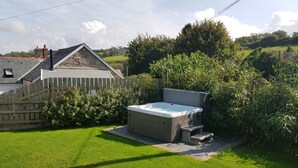 A hot tub in a backyard with a wooden fence, a stone wall, and lush greenery. - Middle Dean Farmhouse (Barnstaple)