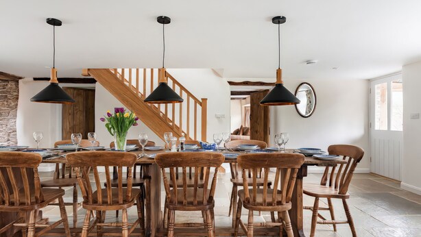A dining area with wooden furniture, black pendant lights, and a staircase in the background. - Middle Dean Farmhouse (Barnstaple)