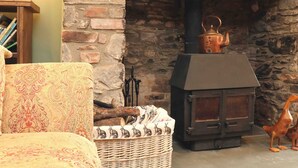 A cozy living room with a stone fireplace, a wicker basket, and a dog. - Middle Dean Farmhouse (Barnstaple)