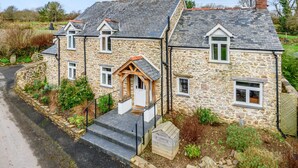 A stone house with a sloped roof, a wooden front porch, and a small garden area. - Middle Dean Farmhouse (Barnstaple)