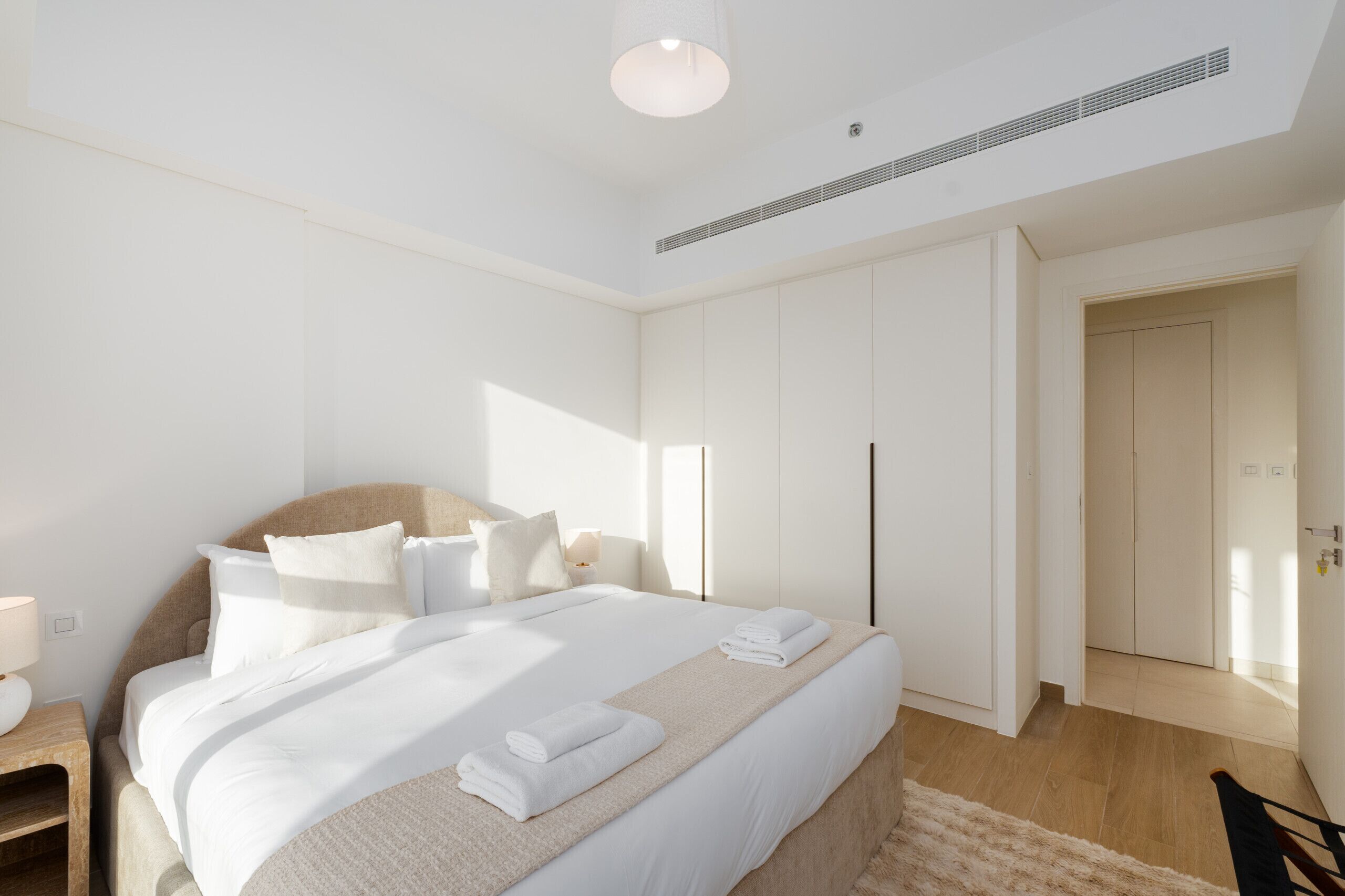A modern bedroom with a large bed, a bedside table, a lamp, and a wardrobe.