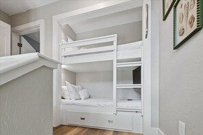 Un lit superposé avec un bureau intégré et un tiroir de rangement, des murs blancs et un escalier menant à un niveau supérieur.