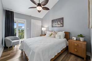 A bedroom with a bed, a chair, a nightstand, a ceiling fan, and a window with curtains. - ENJOY GULF VIEWS from all three decks of this two bedroom townhome. (St. George Island)
