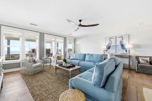A spacious living room with a large window, a ceiling fan, and a view of the ocean. - Welcome to Oyster Bay Escape! (St. George Island)