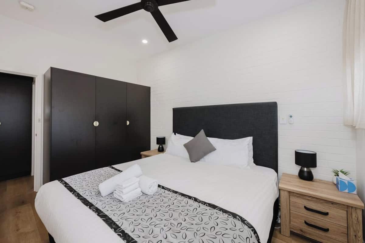 A modern hotel room with a large bed, dark wardrobe, bedside tables, and a ceiling fan.