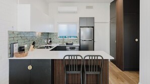 A modern kitchen with a central island, built-in appliances, and a dark wood door. - Palm Beach Villas (Rockingham)