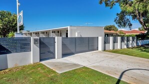 A modern two-story house with a grey exterior, a gated driveway, and a clear blue sky. - Palm Beach Villas (Rockingham)