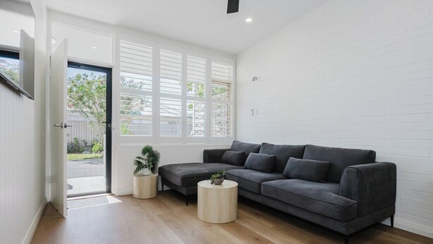 A modern living room with a grey sectional sofa, a small round coffee table, and a potted plant. - Palm Beach Villas (Rockingham)