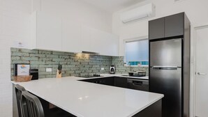 A modern kitchen with white cabinets, a black refrigerator, and a green brick backsplash. - Palm Beach Villas (Rockingham)