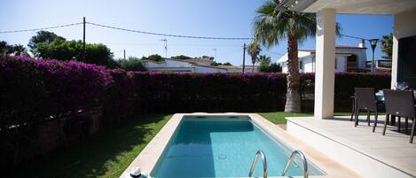 A rectangular swimming pool with a metal ladder, surrounded by a well-maintained lawn and purple flowering bushes.