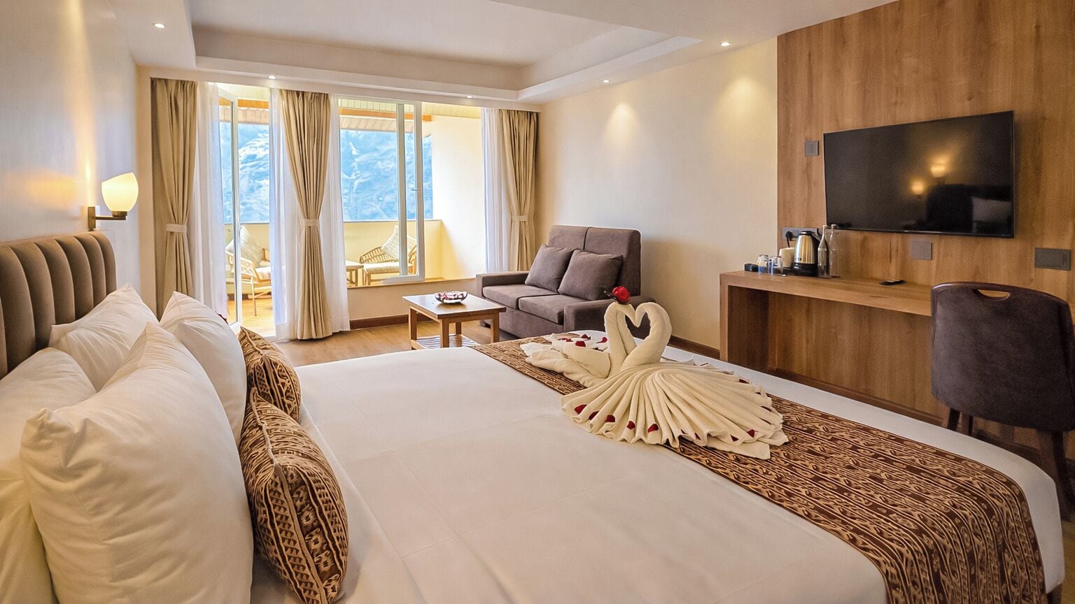 A hotel room with a large bed, a TV, a desk, and a view of the outdoors.
