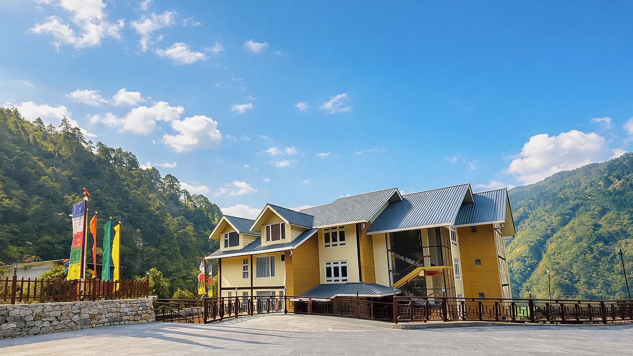 Un immeuble à plusieurs étages, doté d’une façade jaune et d’un toit bleu, entouré d’un mur de pierre et d’une clôture en bois.