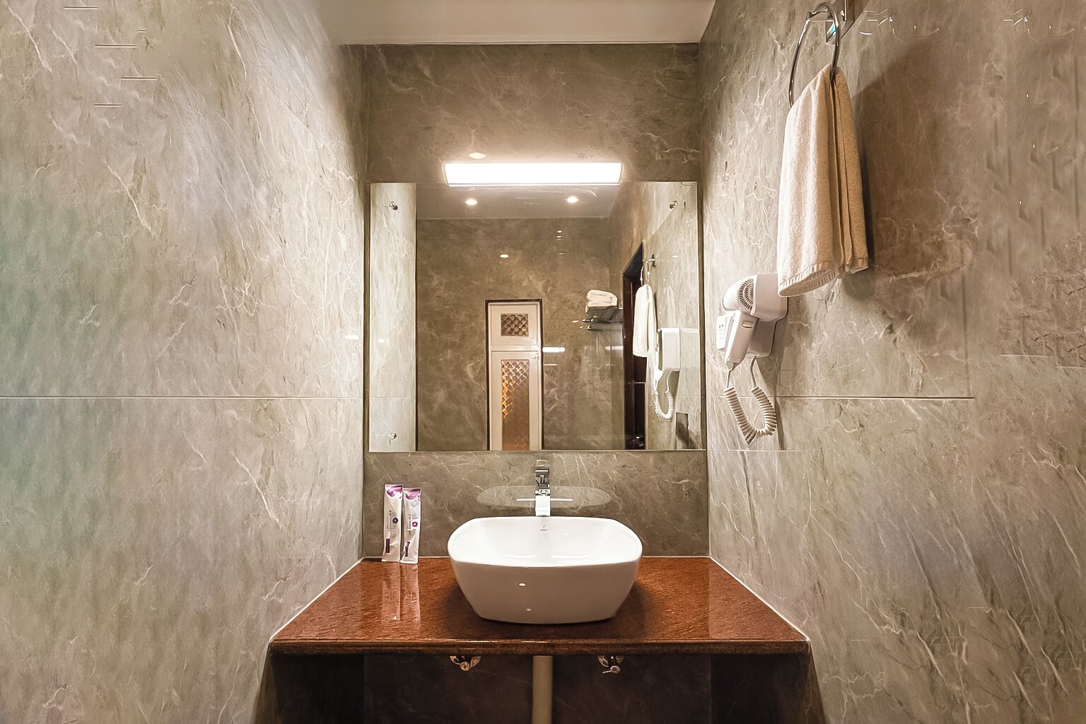 Un baño con pared de mármol, un lavamanos con espejo y un perchero con una toalla.