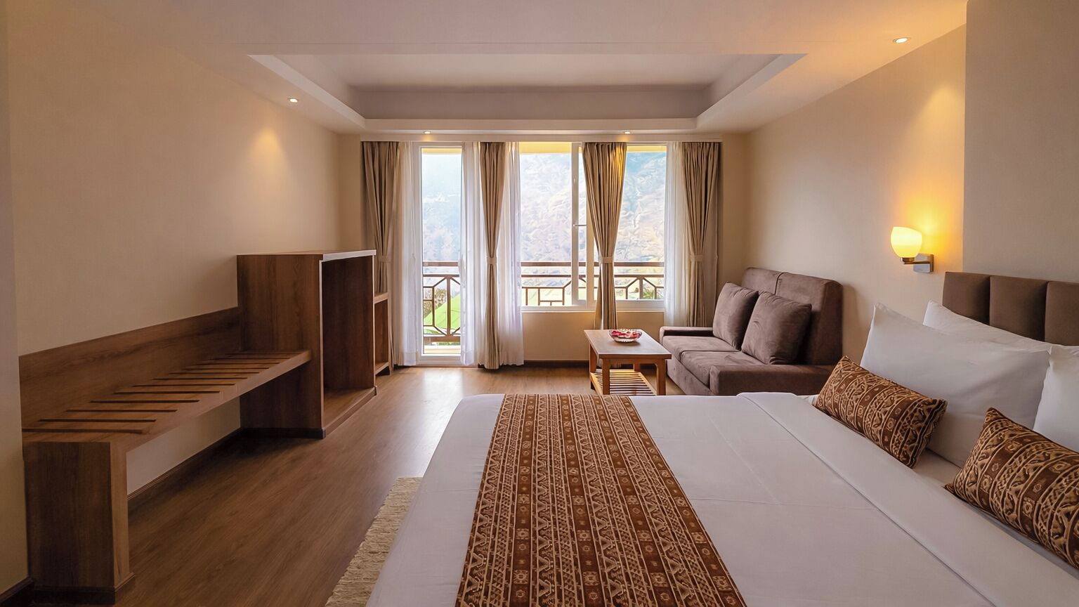 A hotel room with a large bed, a sofa, a TV, and a balcony with curtains.