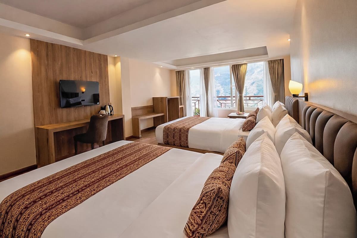 Habitación de hotel con dos camas, televisión montada en la pared, escritorio y balcón con vistas.