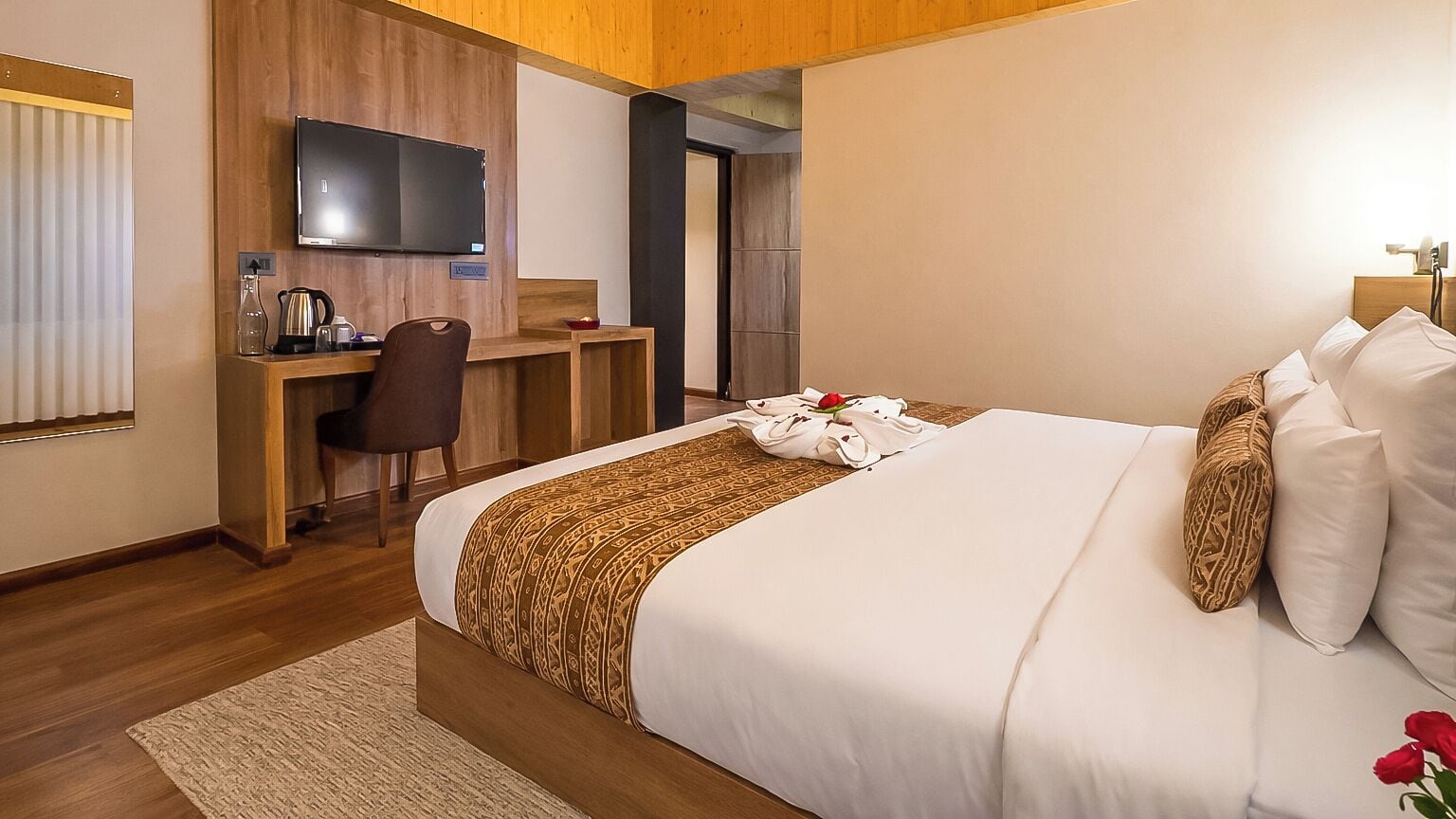 Une chambre d’hôtel avec un grand lit, un bureau, une télévision et un mur décoratif en bois.