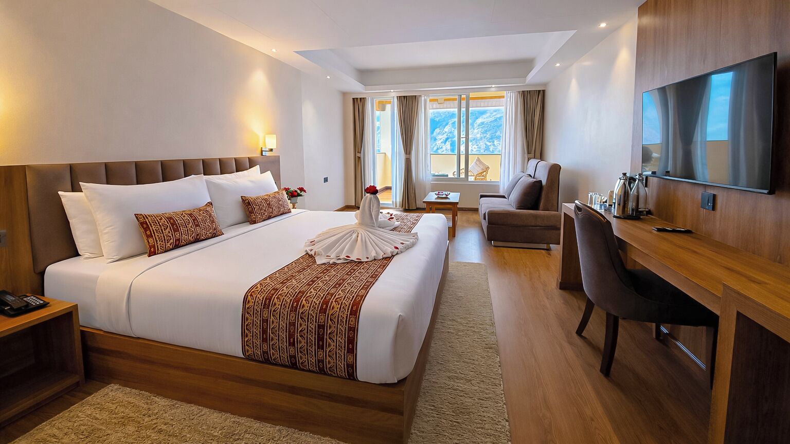 A hotel room with a large bed, a desk, a chair, a TV, and a view of the outdoors.