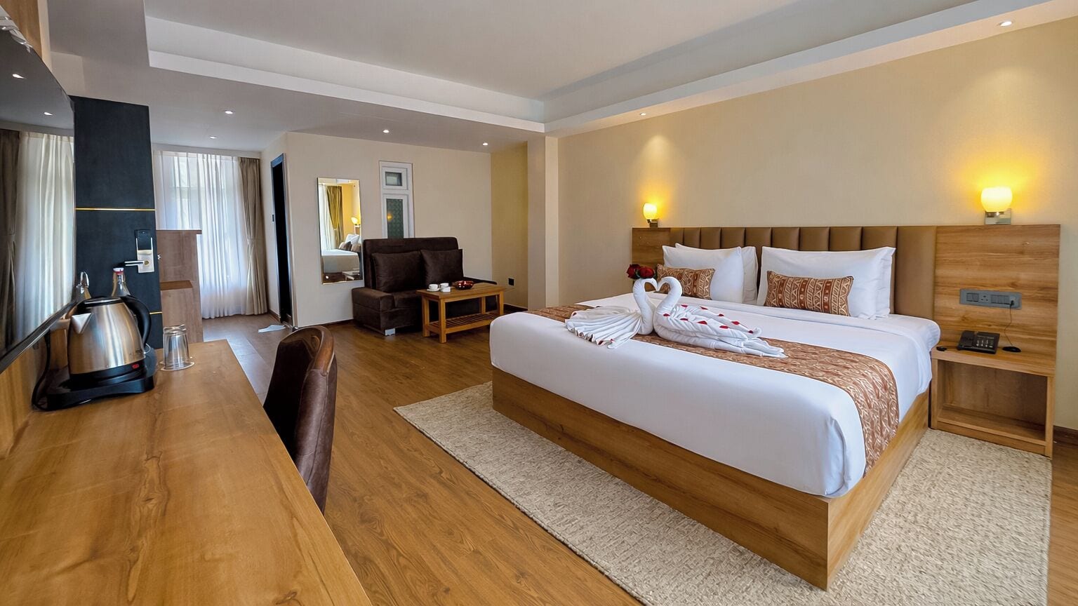Una habitación de hotel con una cama grande, mesitas de noche, un escritorio con hervidor y una silla.