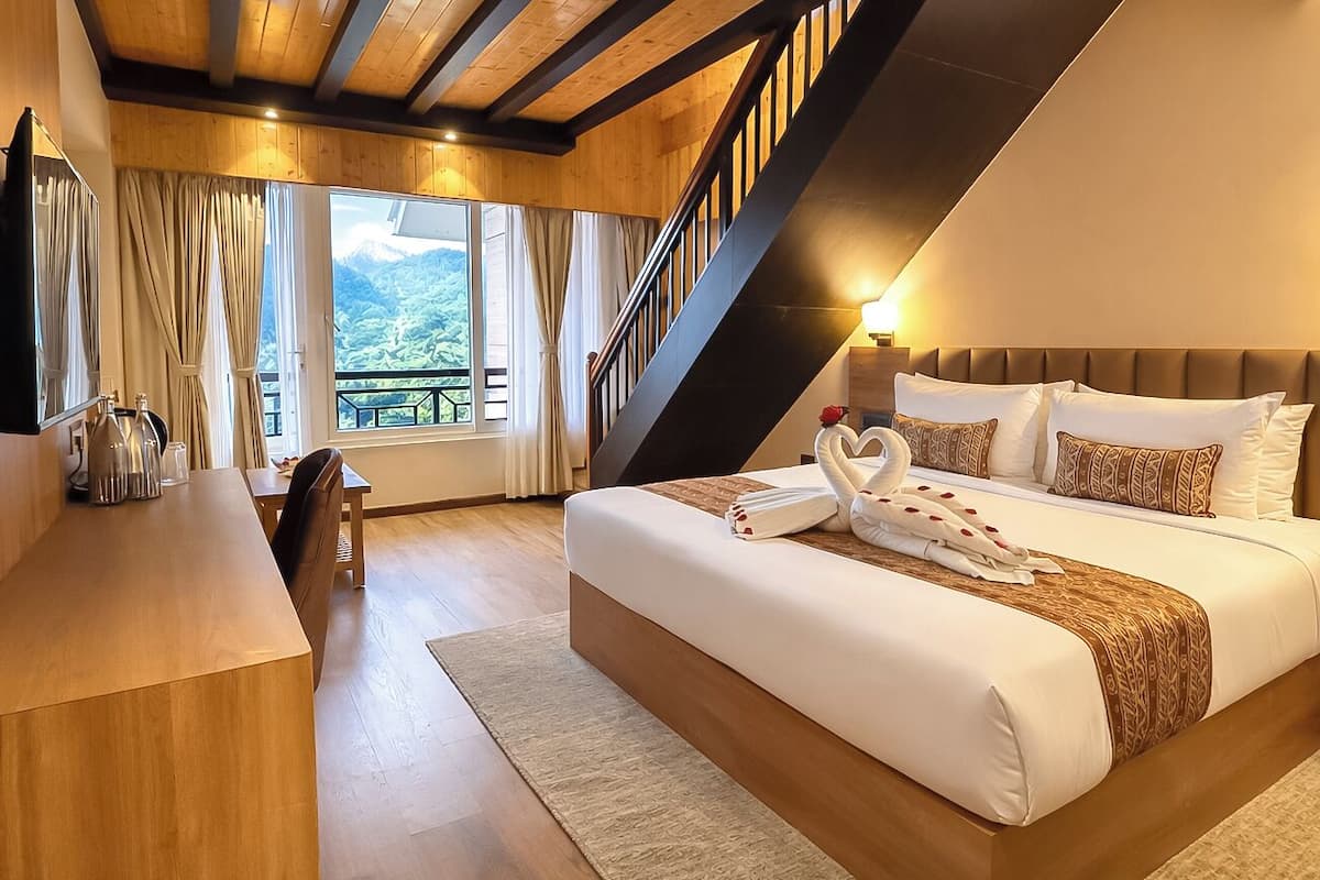 Una habitación de hotel moderna con una cama grande, muebles de madera, un escritorio y vistas a las montañas a través de la ventana.