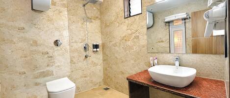 A bathroom with a marble wall, a white toilet, a shower, a sink with a mirror, and a hairdryer.