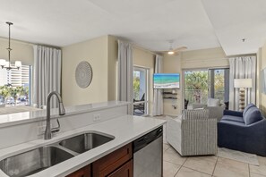 A modern kitchen with a double sink, a dishwasher, and a dining area with a view of the beach. - Book 3 Nights & Get 1 Free/See Description* Walk to Beach & Pool* Tiki Bar* Tram (Miramar Beach)