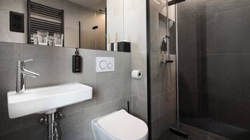 A modern bathroom with a white sink, a toilet, and a glass-enclosed shower.